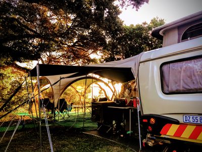 A caravan and awning pitched under coastal trees at golden hour